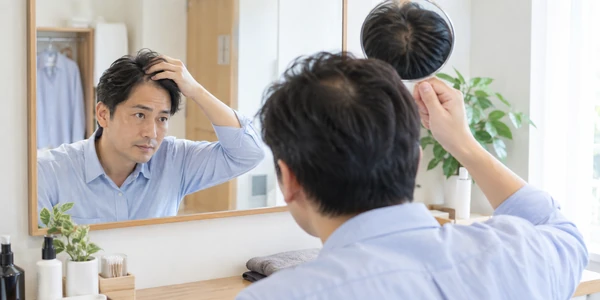 鏡で頭頂部と生え際を確認する日本人男性